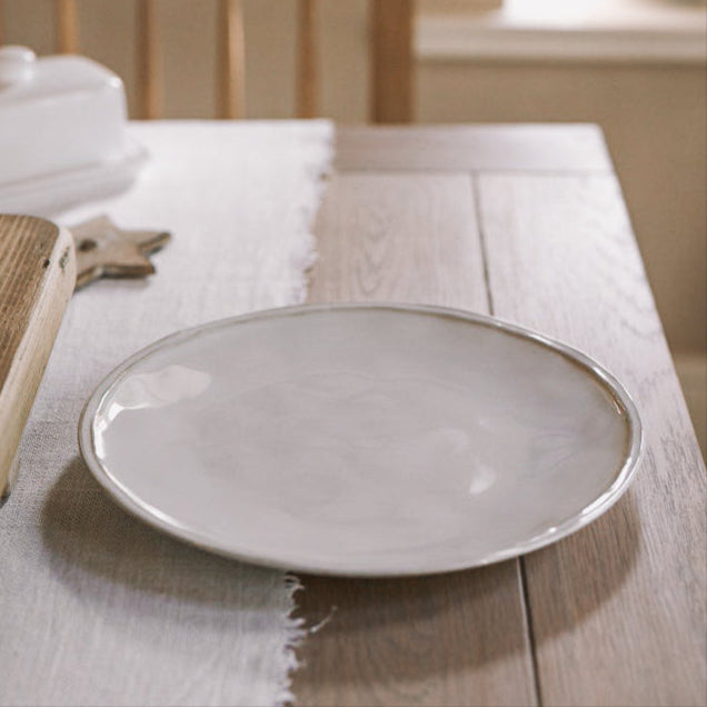 white ceramic dinner plate on wooden table with white table runner.