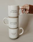 Stack of white and brown natural stoneware mugs with black slogans.