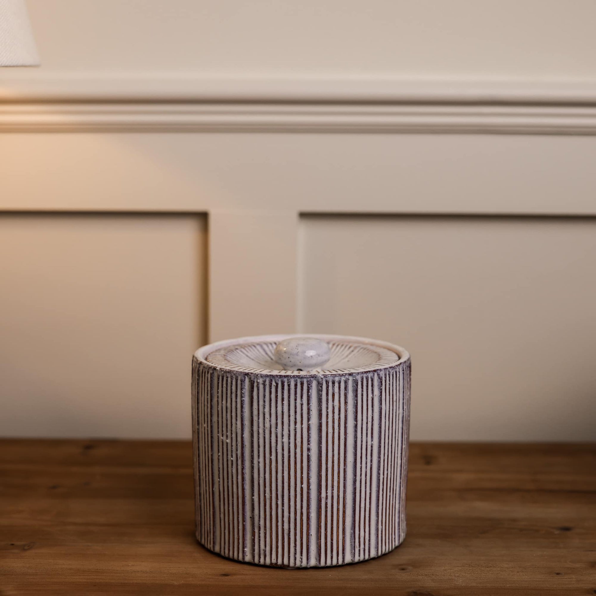 Small red and white striped ceramic storage jar on wooden console.