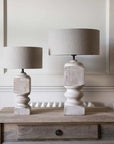 Large and small white washed mango wood table lamps on a wooden desk against a panelled wall. 