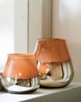 Caramel and silver tealight holder with larger one behind, and lit candle inside.