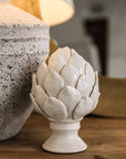 White ceramic artichoke ornament on console with stone lamp.