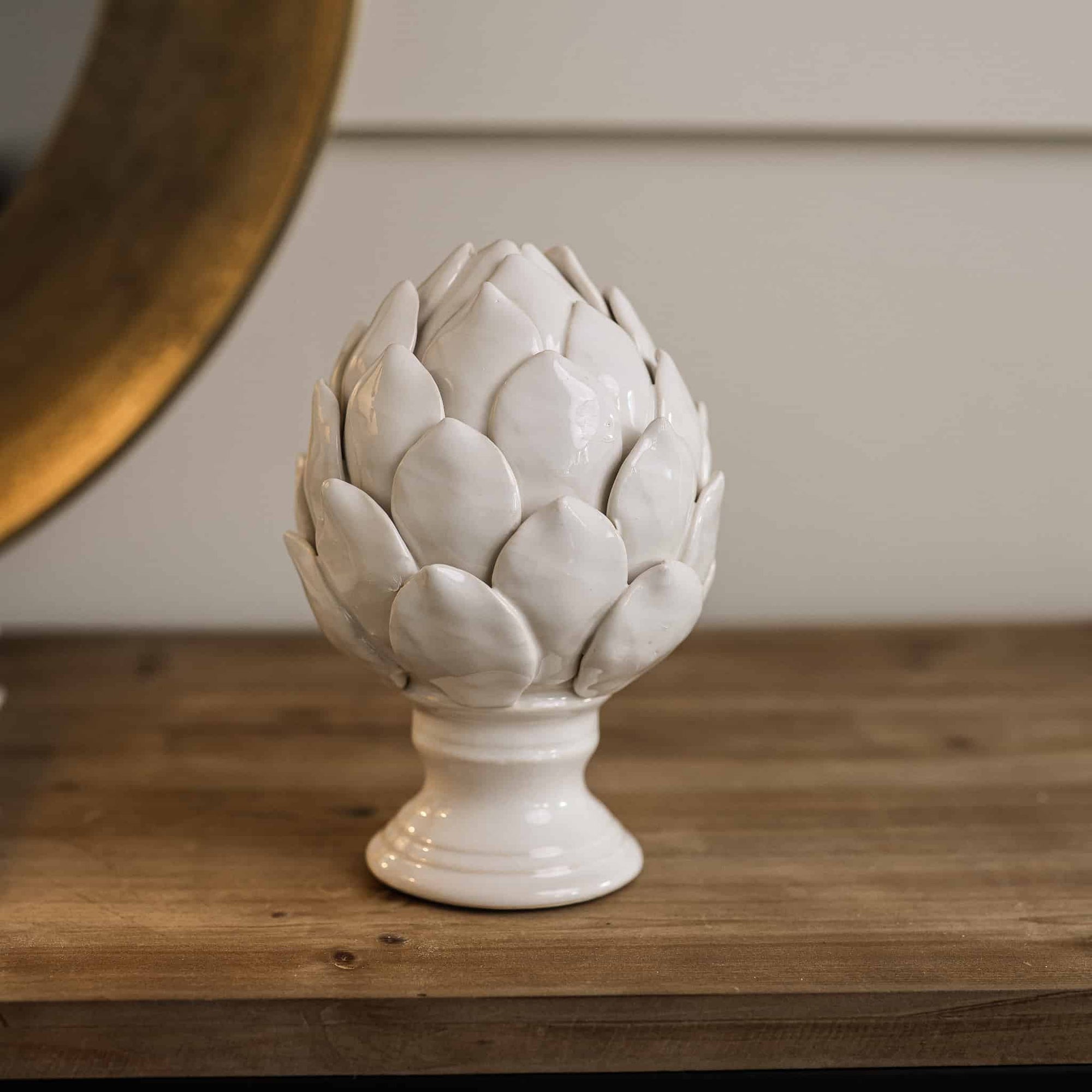 White ceramic artichoke ornament on stand on wooden console.