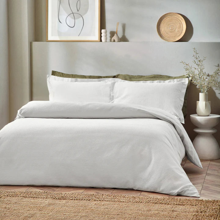 White waffle bedding set on double bed with green pillows.