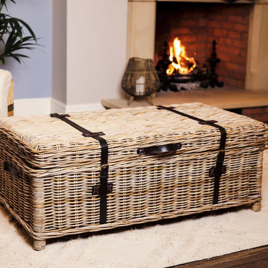 Wicker basket coffee table in front of lit fire on white rug.