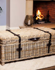 Wicker basket coffee table in front of lit fire on white rug.
