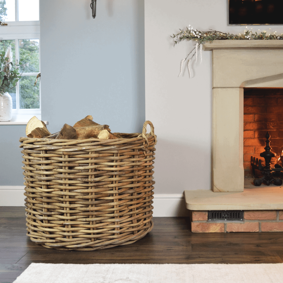 Large rattan log basket filled with firewood in front of a fire.