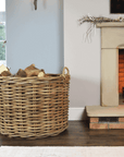 Large rattan log basket filled with firewood in front of a fire.