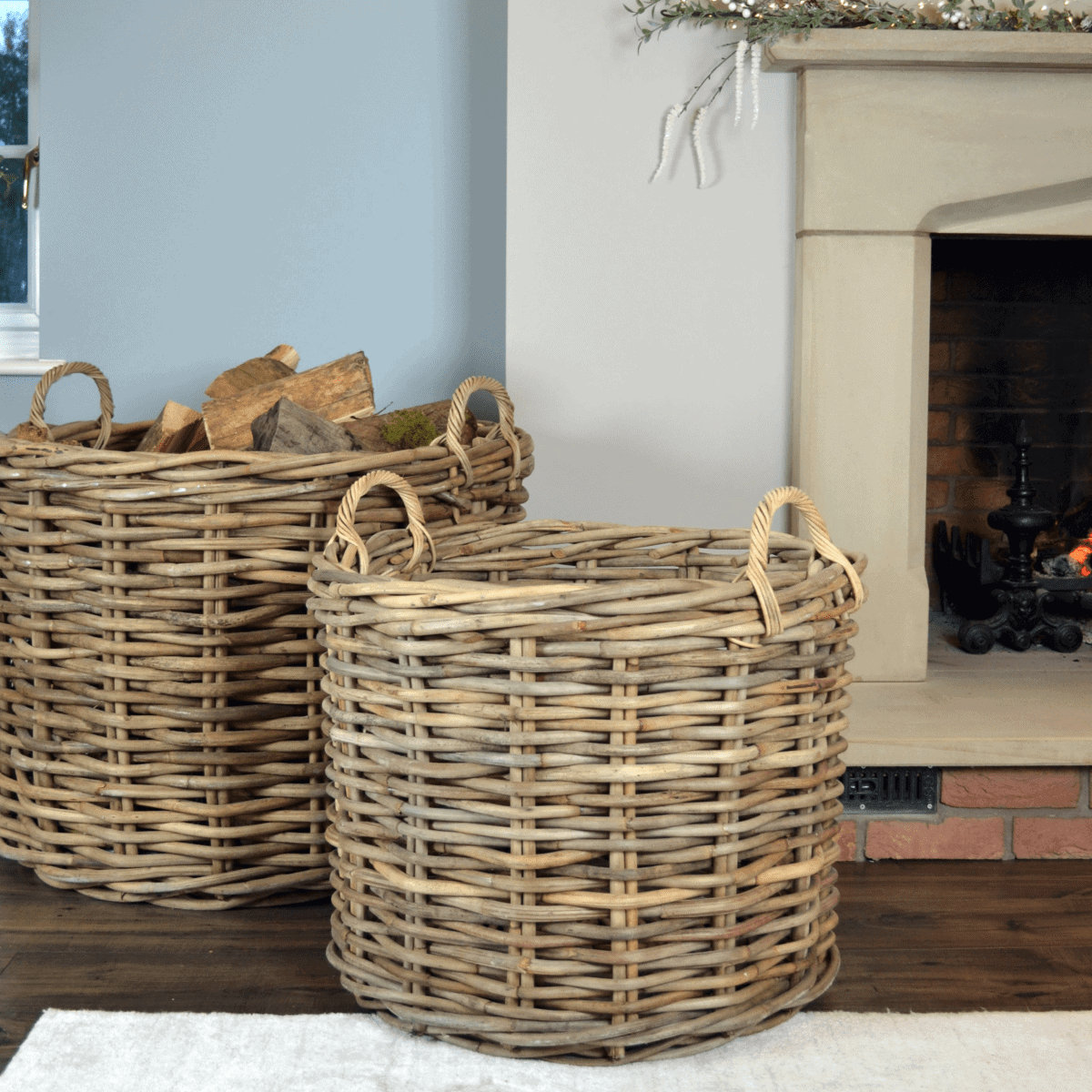 2 large rattan log baskets in front of fire, one filled with logs.