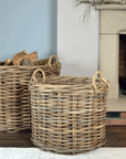 2 large rattan log baskets in front of fire, one filled with logs.