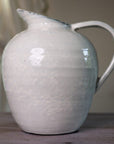 White ceramic vase with blue hued ceramic glaze, from the side on wooden table.