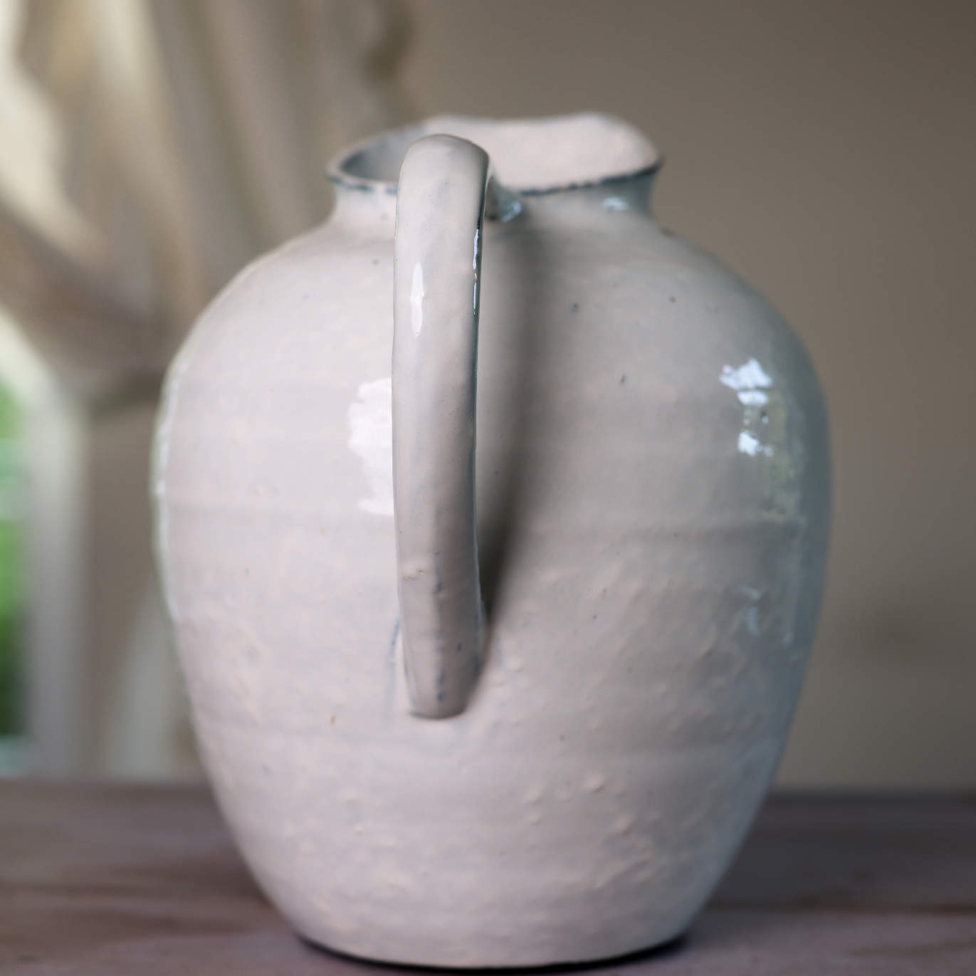 White ceramic vase with blue hued ceramic glaze, handle close up on wooden table.