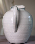 White ceramic vase with blue hued ceramic glaze, handle close up on wooden table.