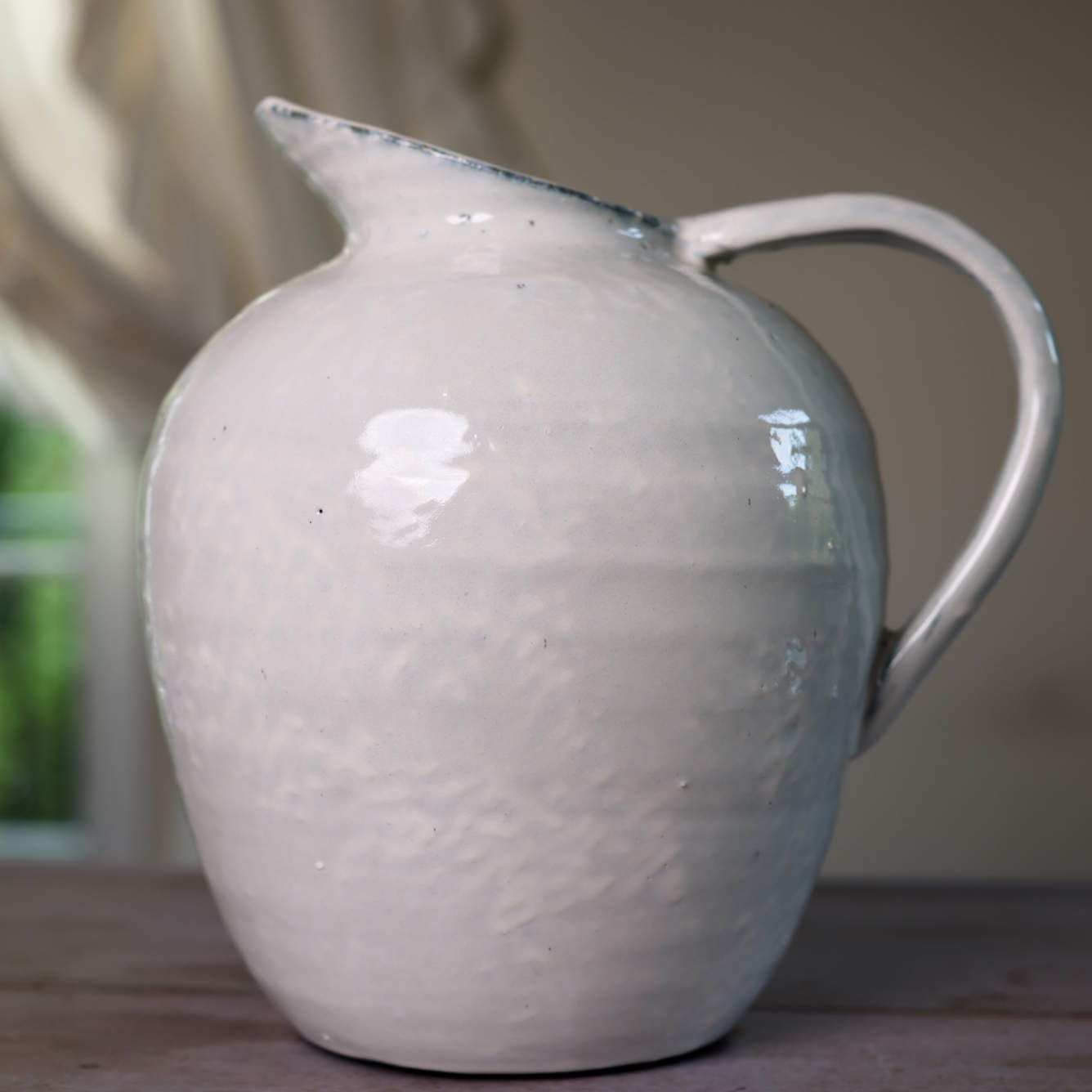 White ceramic vase with blue hued ceramic glaze, from the side close up on wooden table.