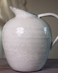White ceramic vase with blue hued ceramic glaze, from the side close up on wooden table.