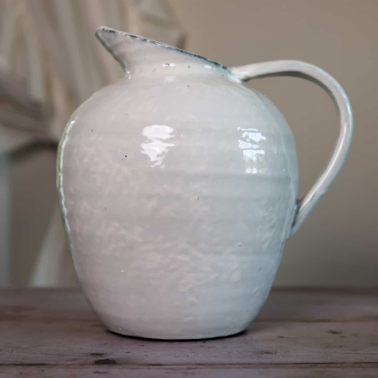 White ceramic vase with blue hued ceramic glaze, close up from the side on wooden table.