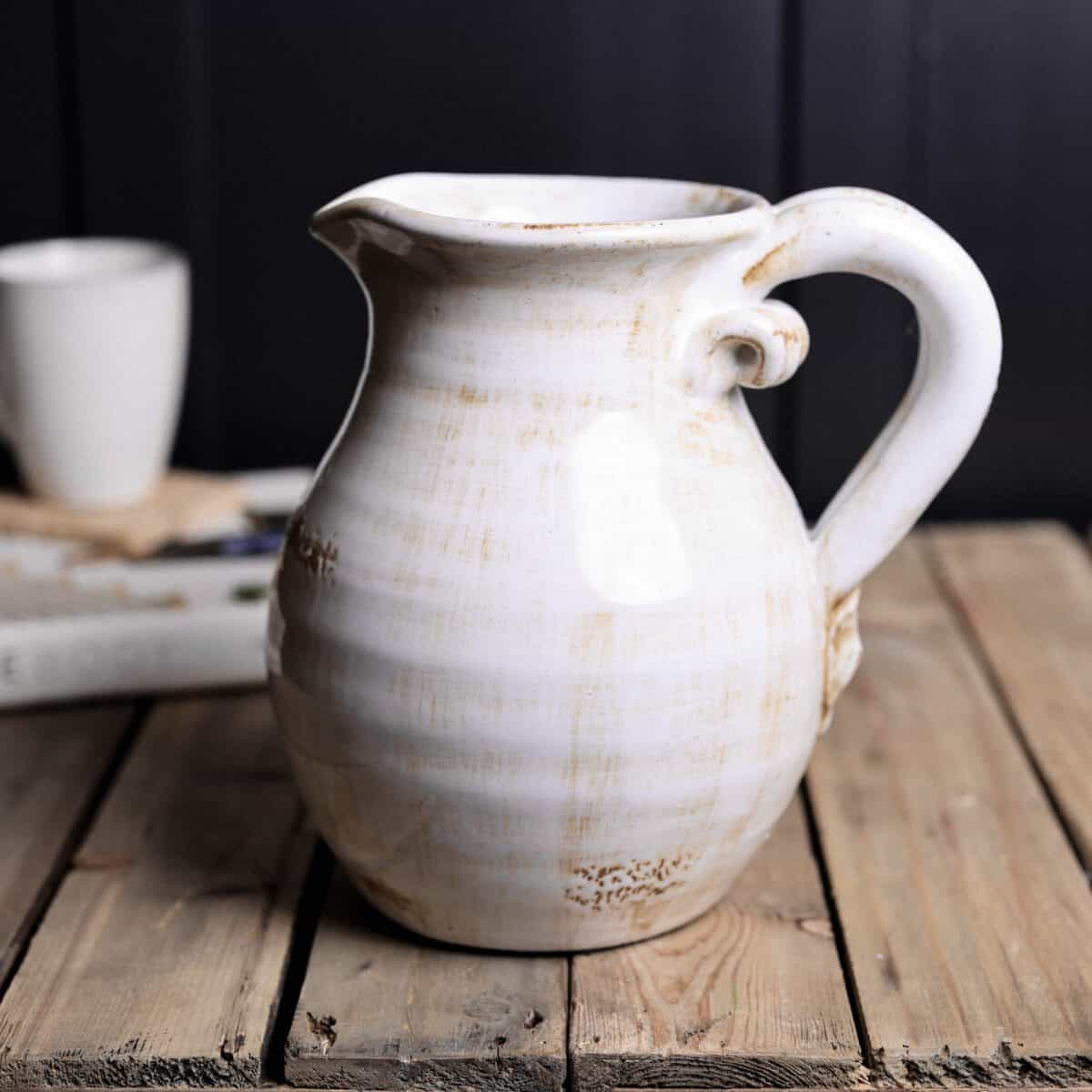 Off white jug with handle on wooden table.