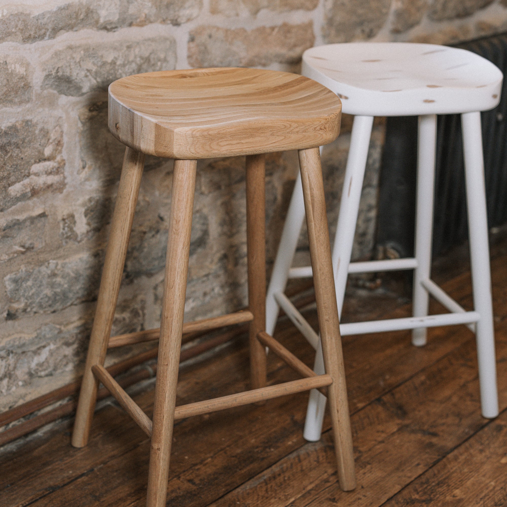 Natural wooden and white wooden backless barstools against stone wall.