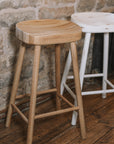 Natural wooden and white wooden backless barstools against stone wall.