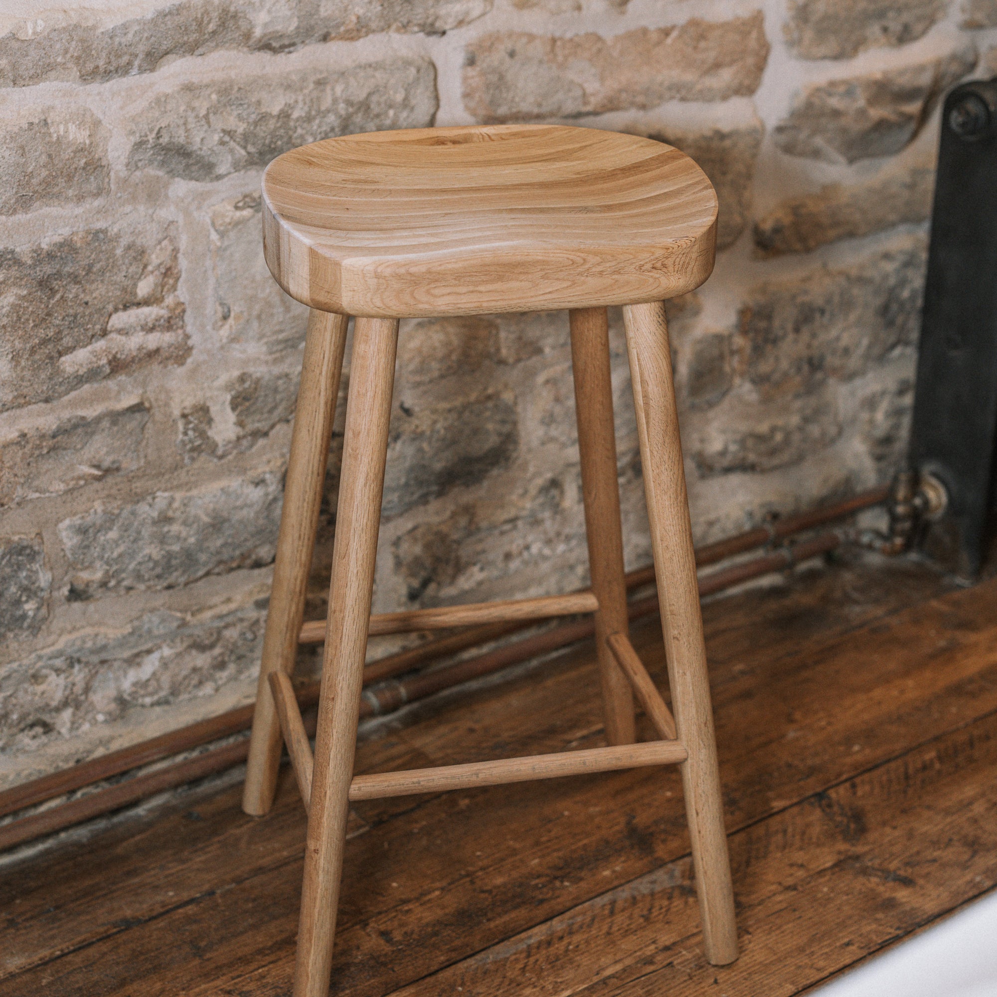 Natural wooden backless barstool against stone wall.