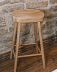 Natural wooden backless barstool against stone wall.