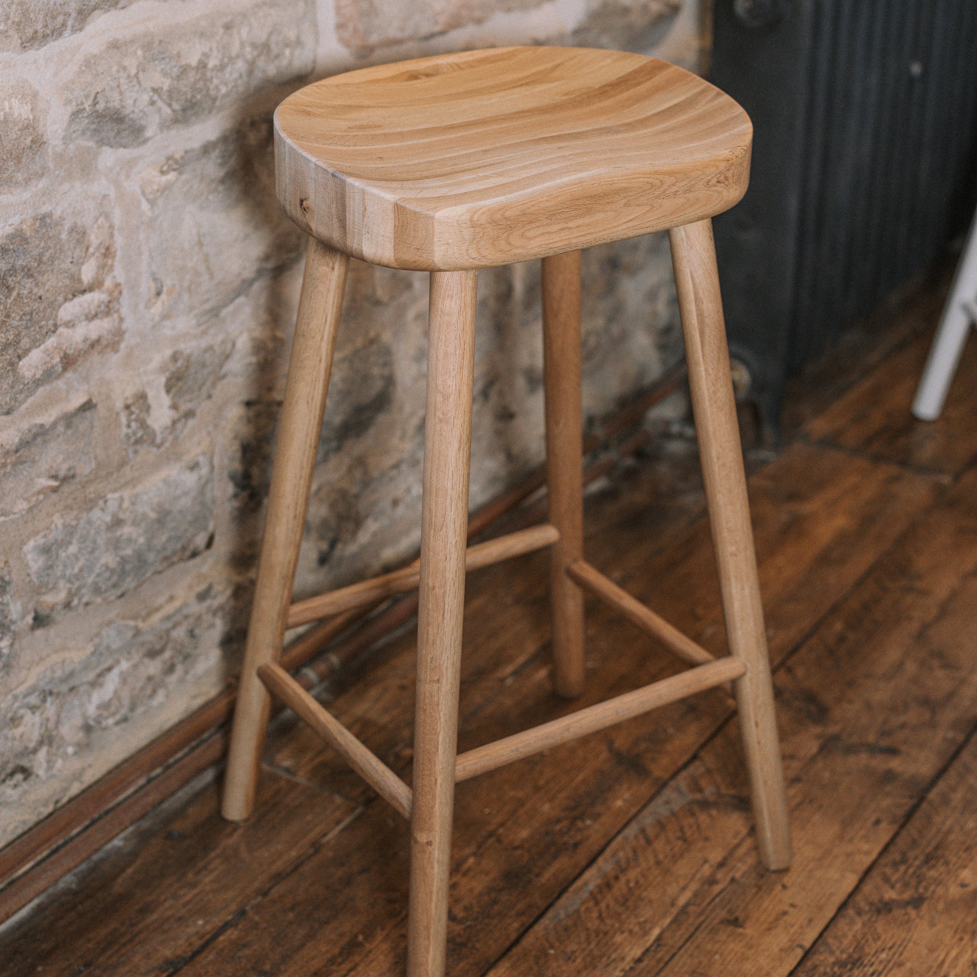 Natural wooden backless barstool against stone wall.