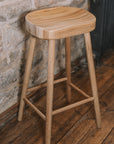 Natural wooden backless barstool against stone wall.