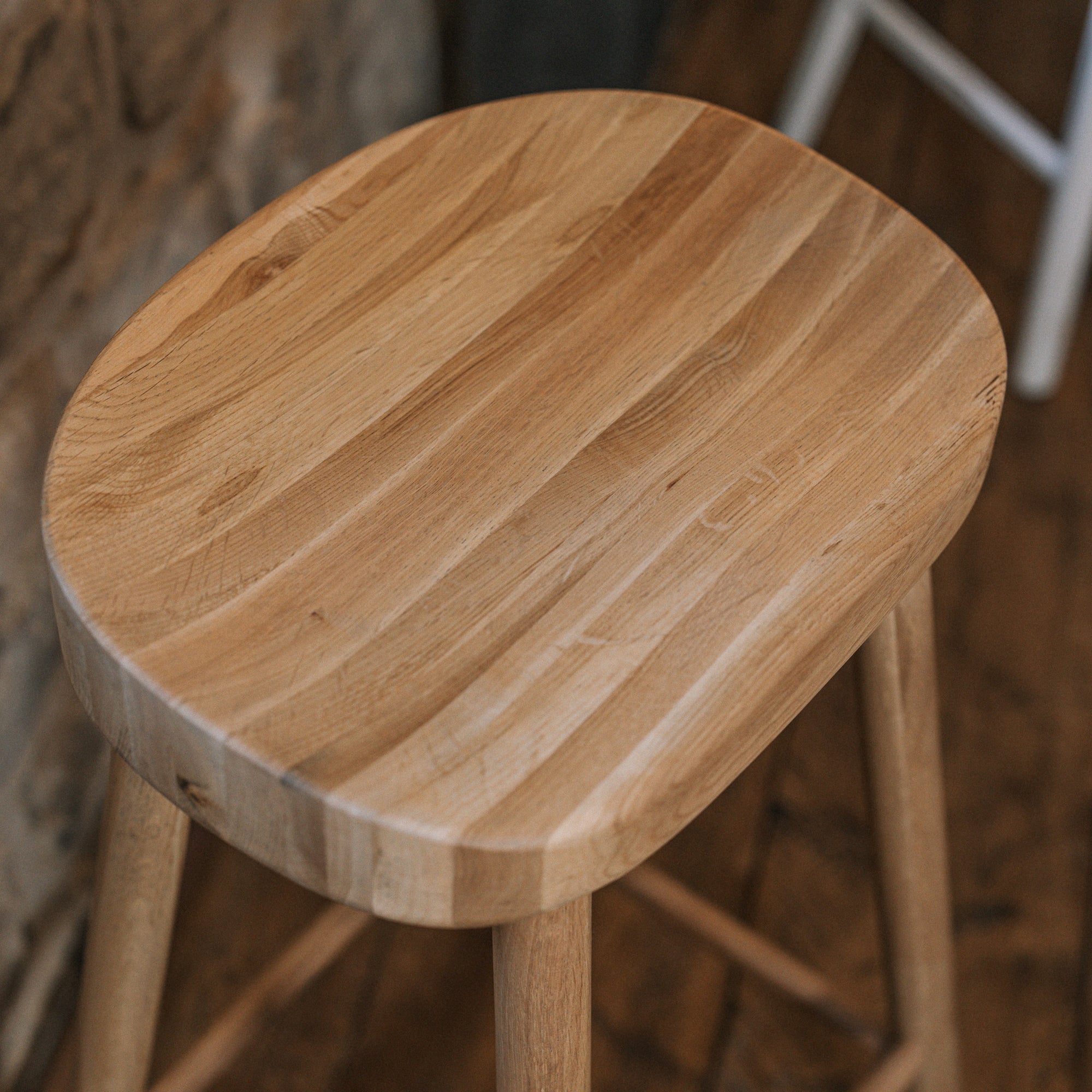 Natural wooden backless barstool against stone wall.