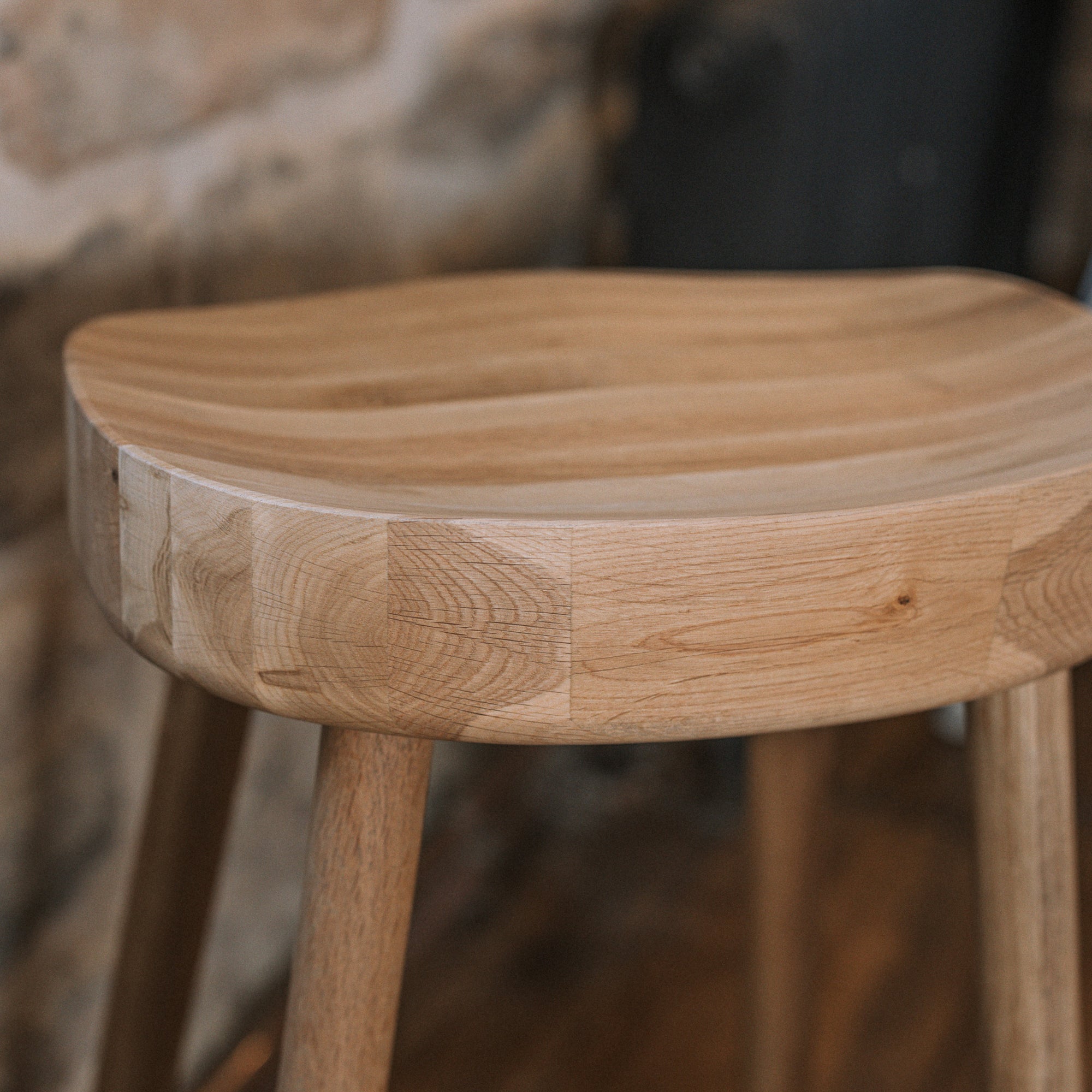 A detailed shot of a natural wooden backless barstool against stone wall.