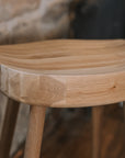 A detailed shot of a natural wooden backless barstool against stone wall.