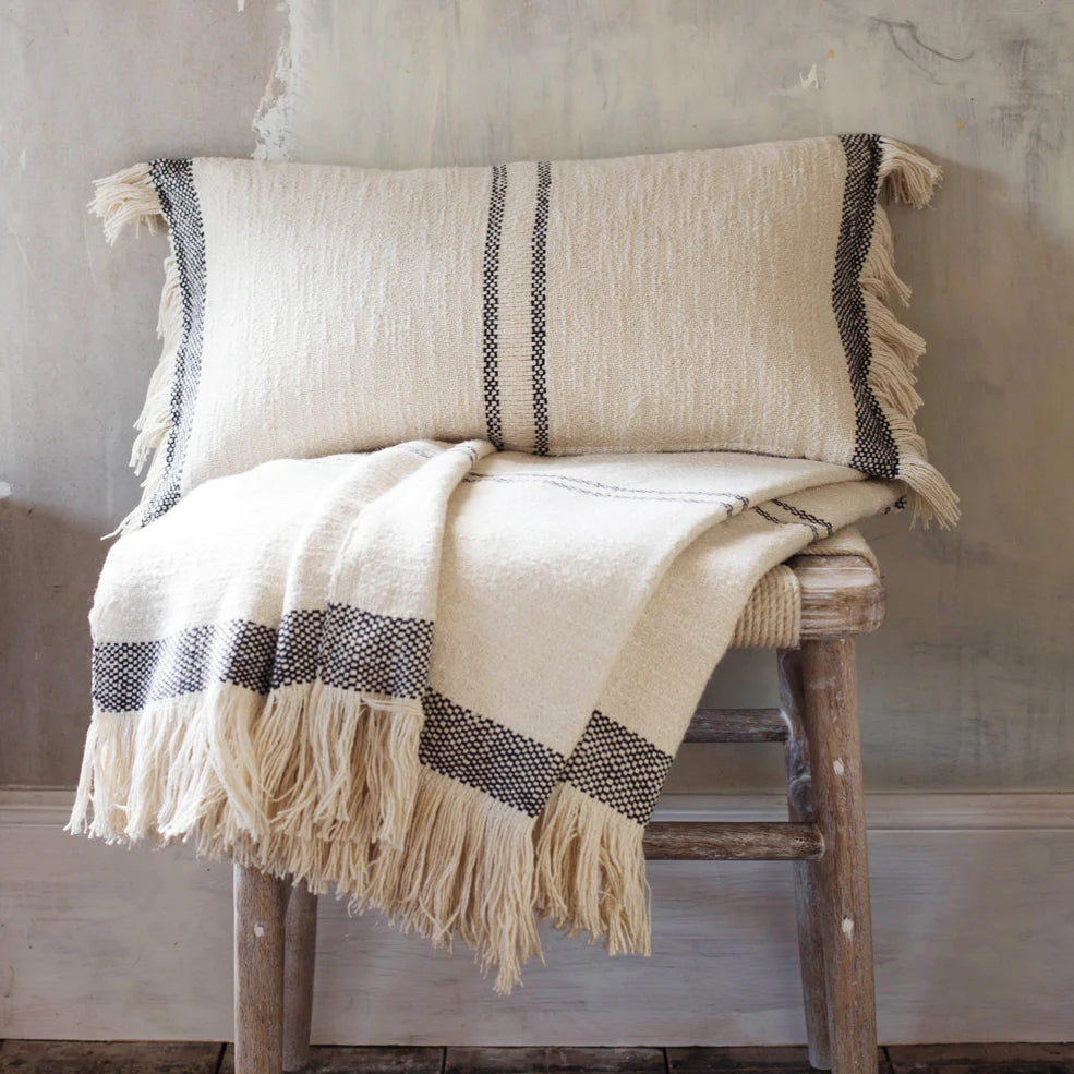 Andas cotton cushion and throw blanket on a rustic wooden stool.