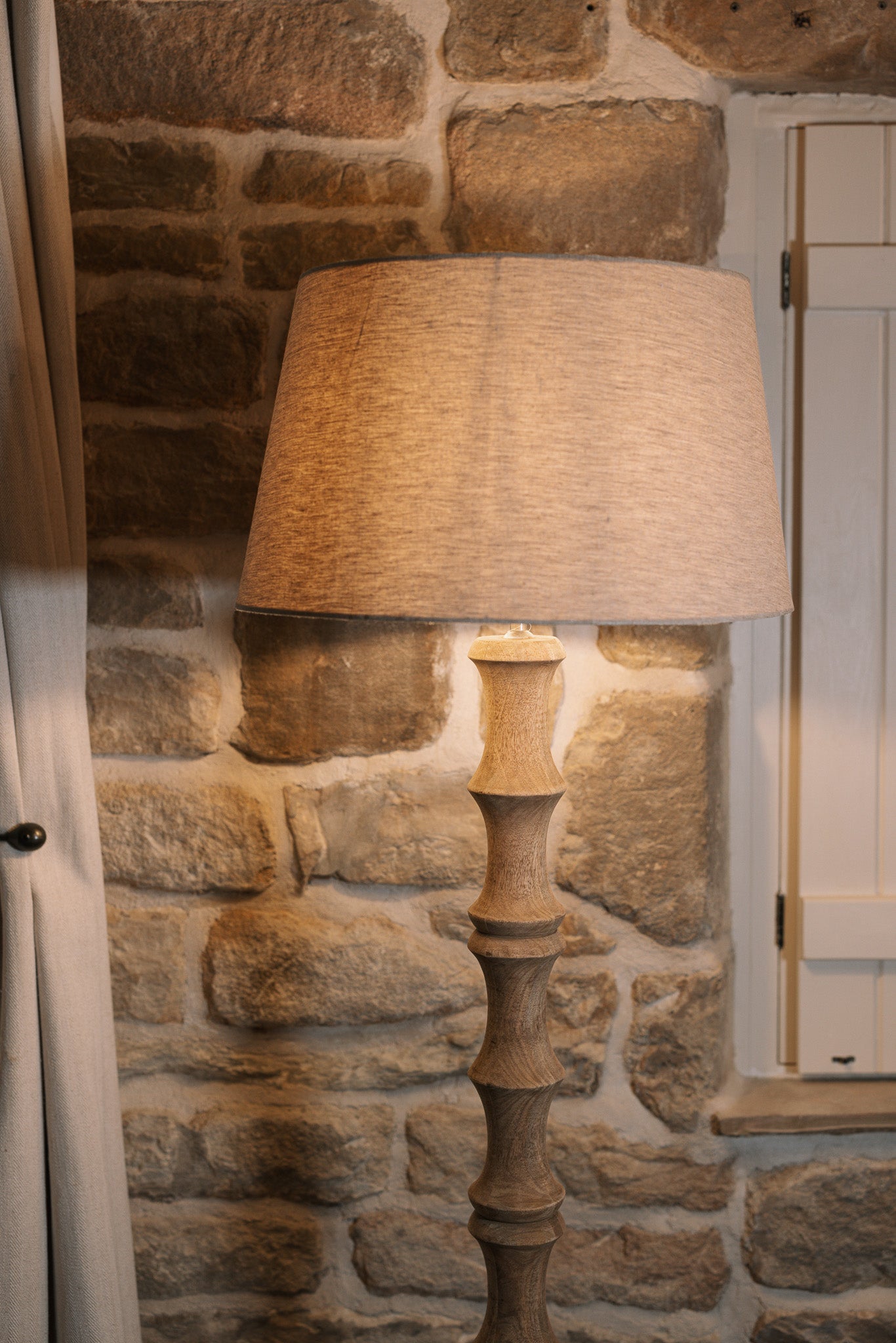 Bamboo look wooden floor lamp with linen shade against stone wall.