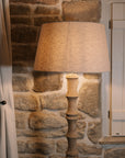 Bamboo look wooden floor lamp with linen shade against stone wall.