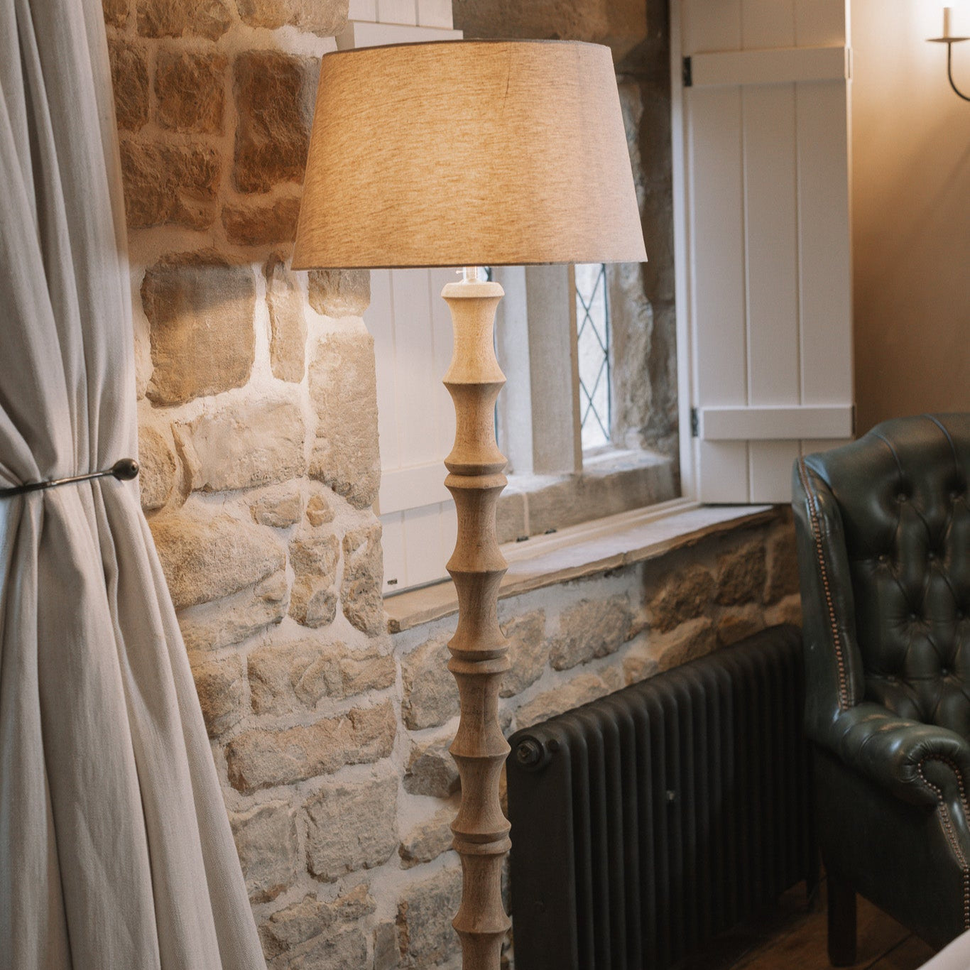 Bamboo look wooden floor lamp with linen shade against stone wall.