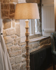 Bamboo look wooden floor lamp with linen shade against stone wall.