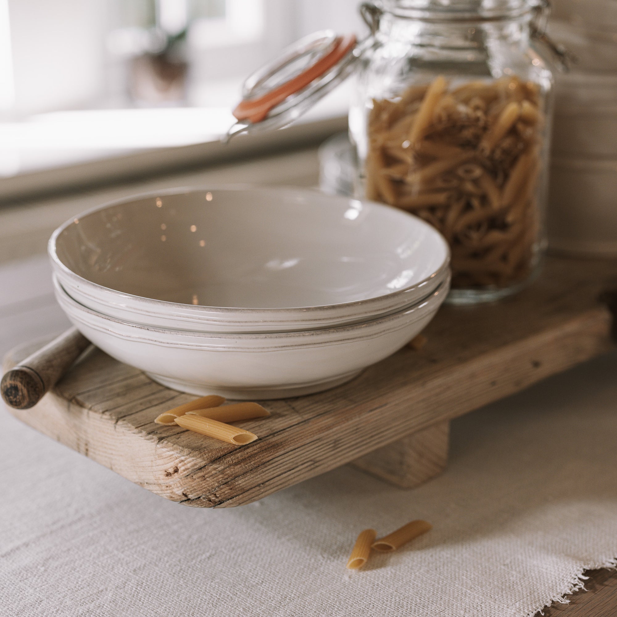 Ceramic pasta plate on wooden table with jar of dried penne.