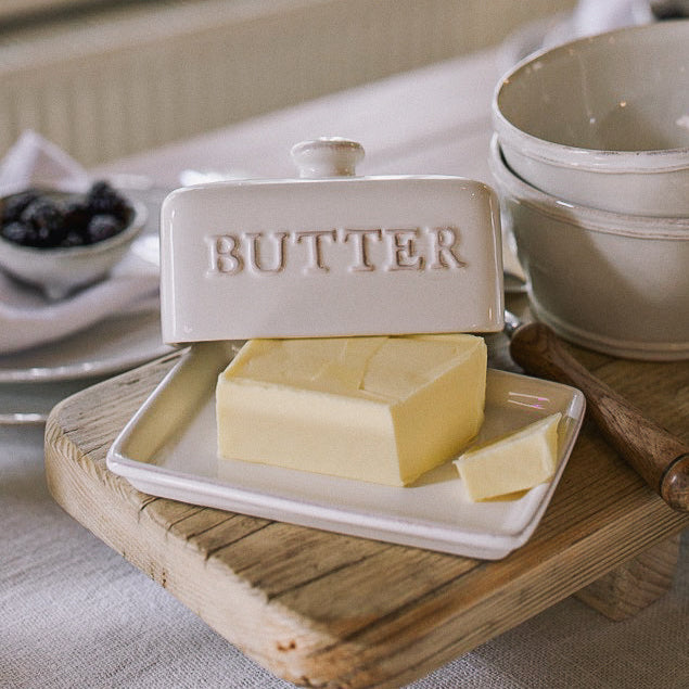 Ceramic butter dish with embossed 'butter' name, and block of butter on wooden serving board.