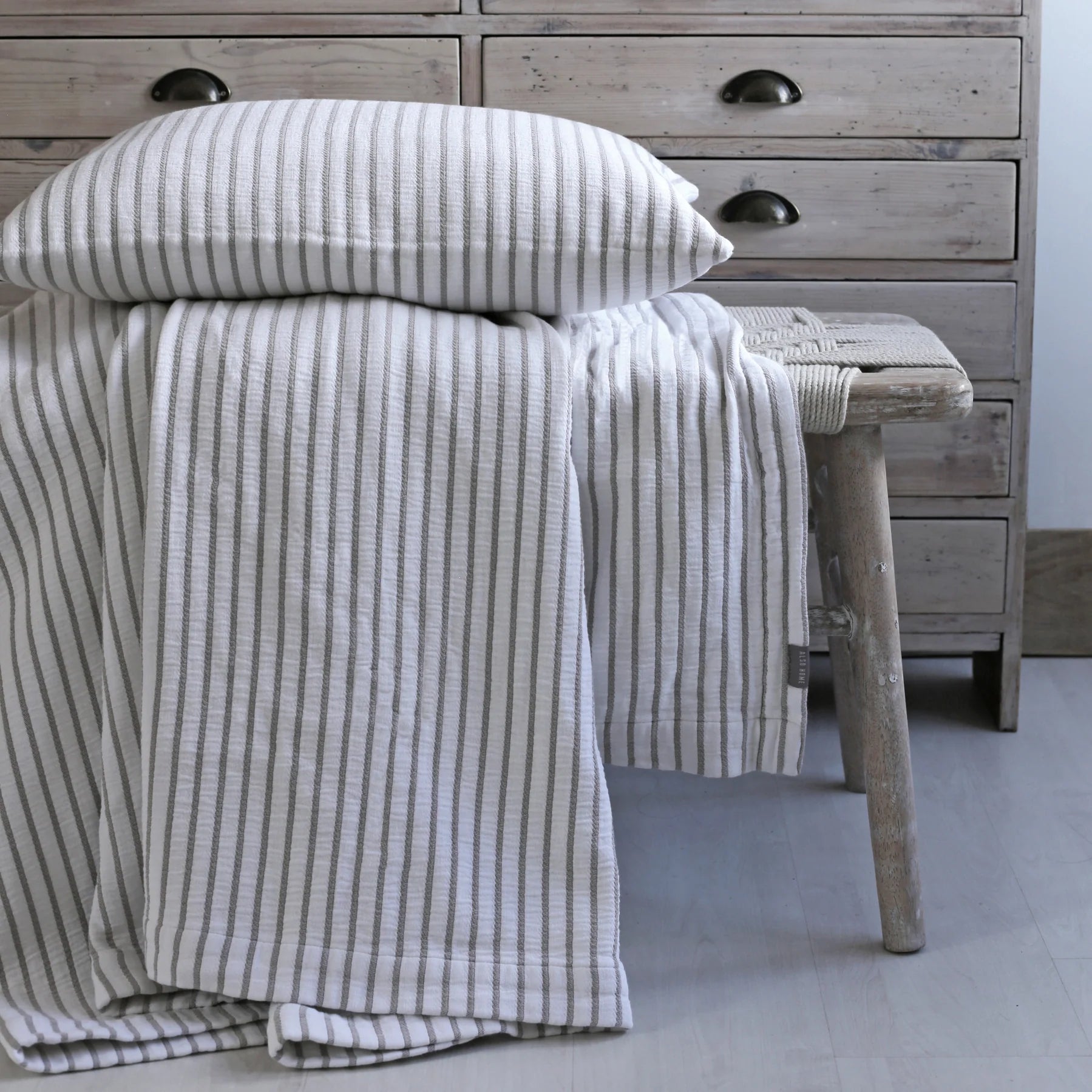 A Striped Cotton Throw Blanket and cushion on a woven bench.