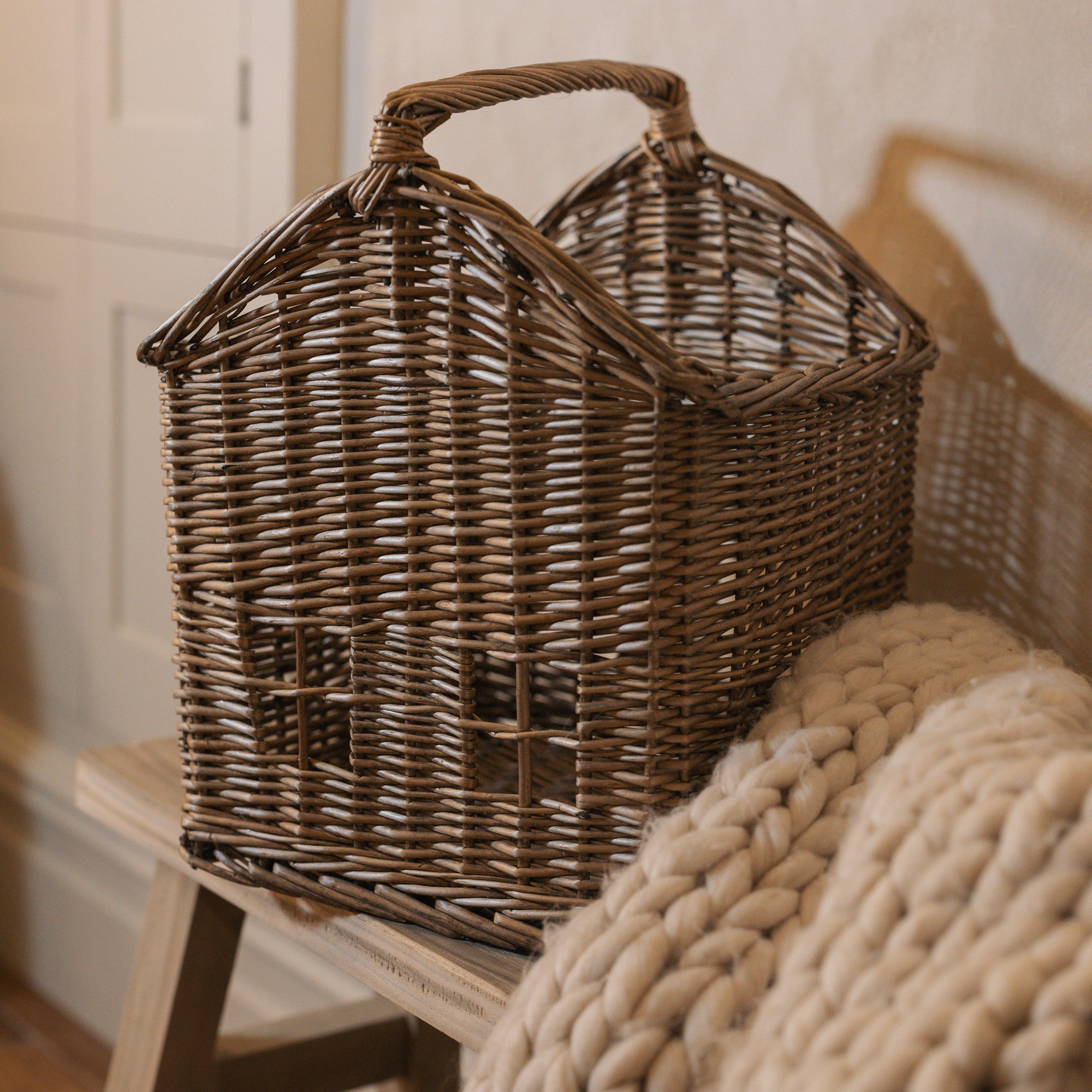 Woven basket with handle with chunky knitted throw on wooden bench.