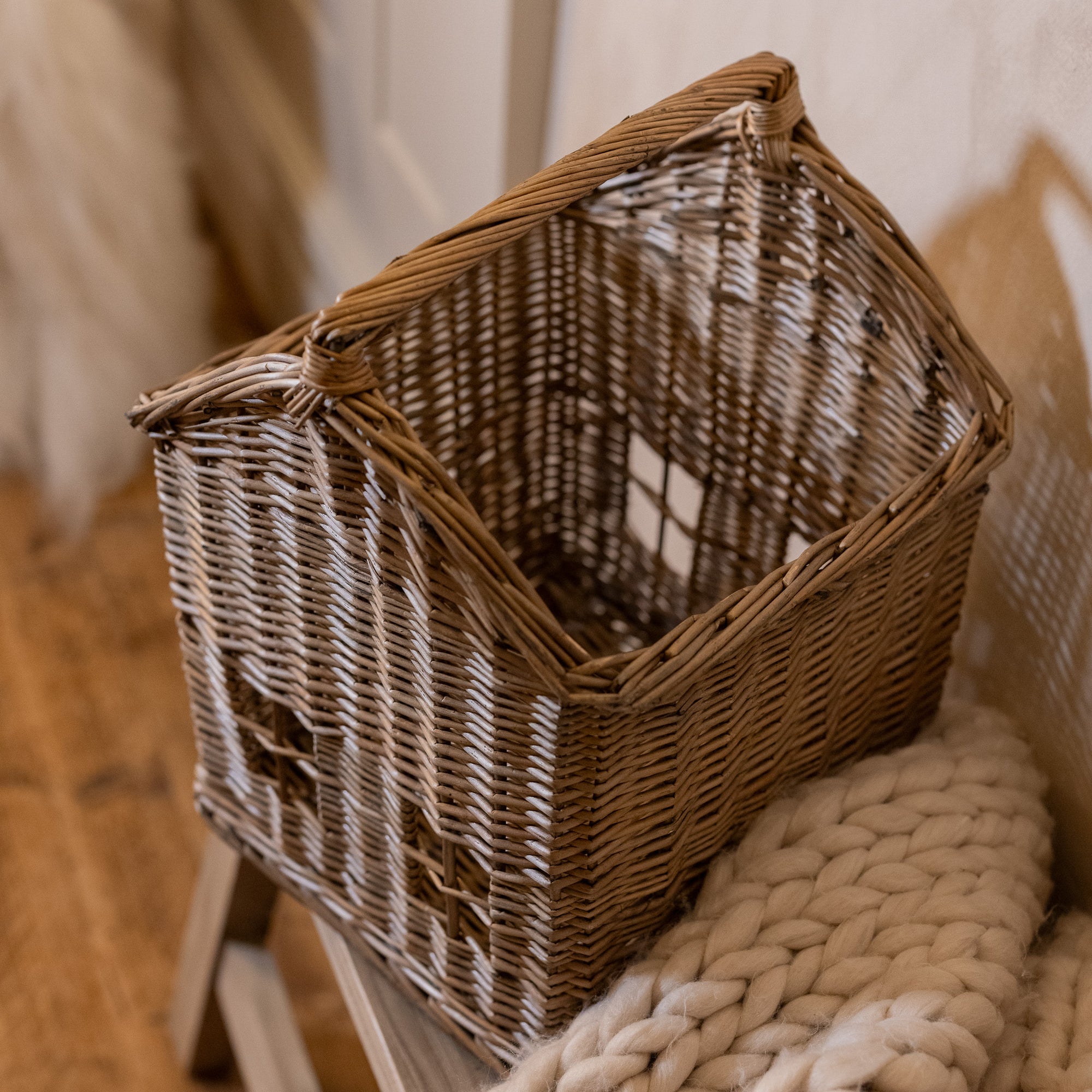 Woven basket with handle with chunky knitted throw on wooden bench.