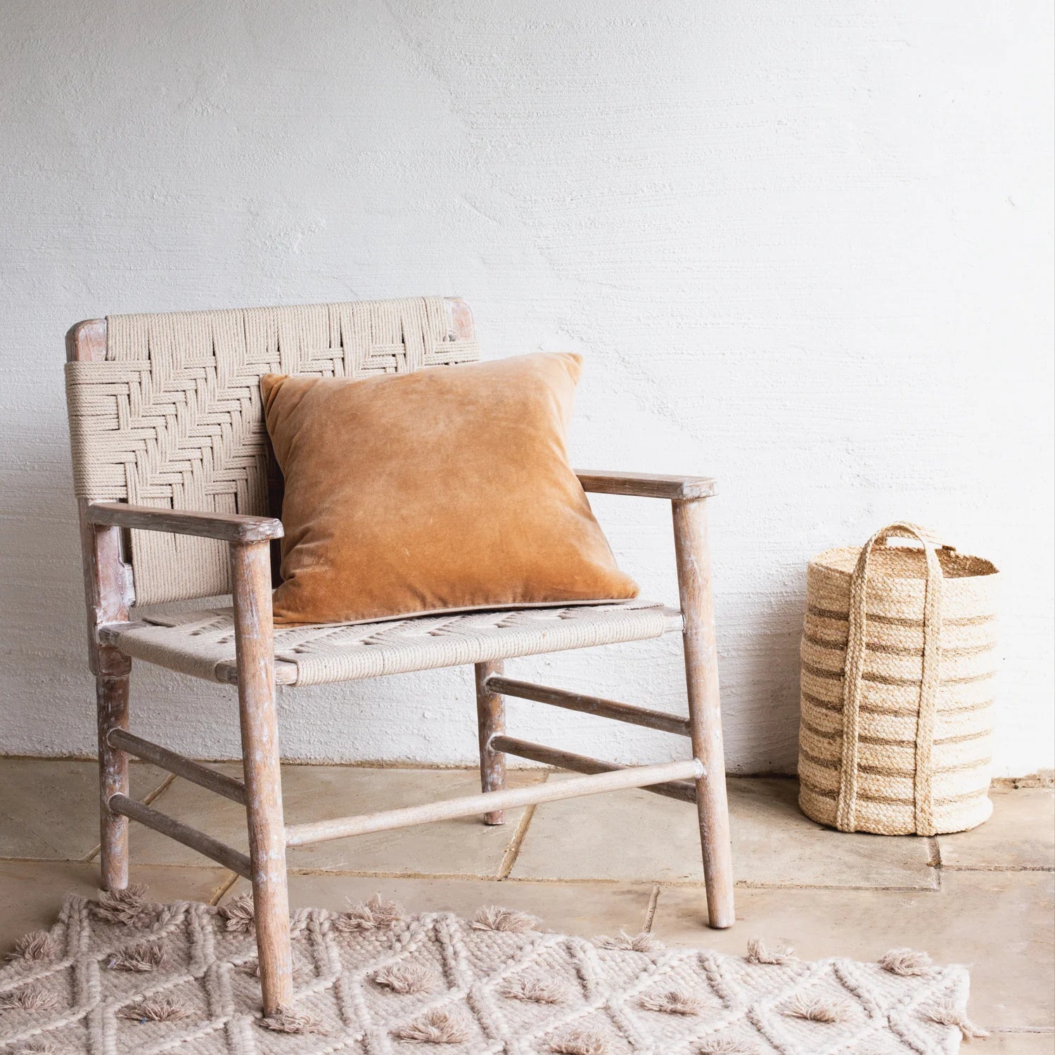 The Lulworth Rustic Wooden Armchair styled with an orange velvet cushion and a small basket.