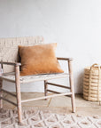 The Lulworth Rustic Wooden Armchair styled with an orange velvet cushion and a small basket.