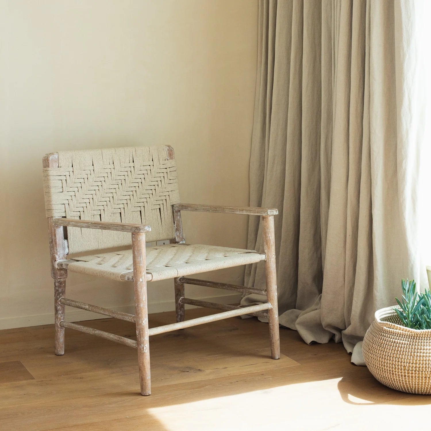 The Lulworth Rustic Wooden Armchair in a neutral living room with a small basket and plant.