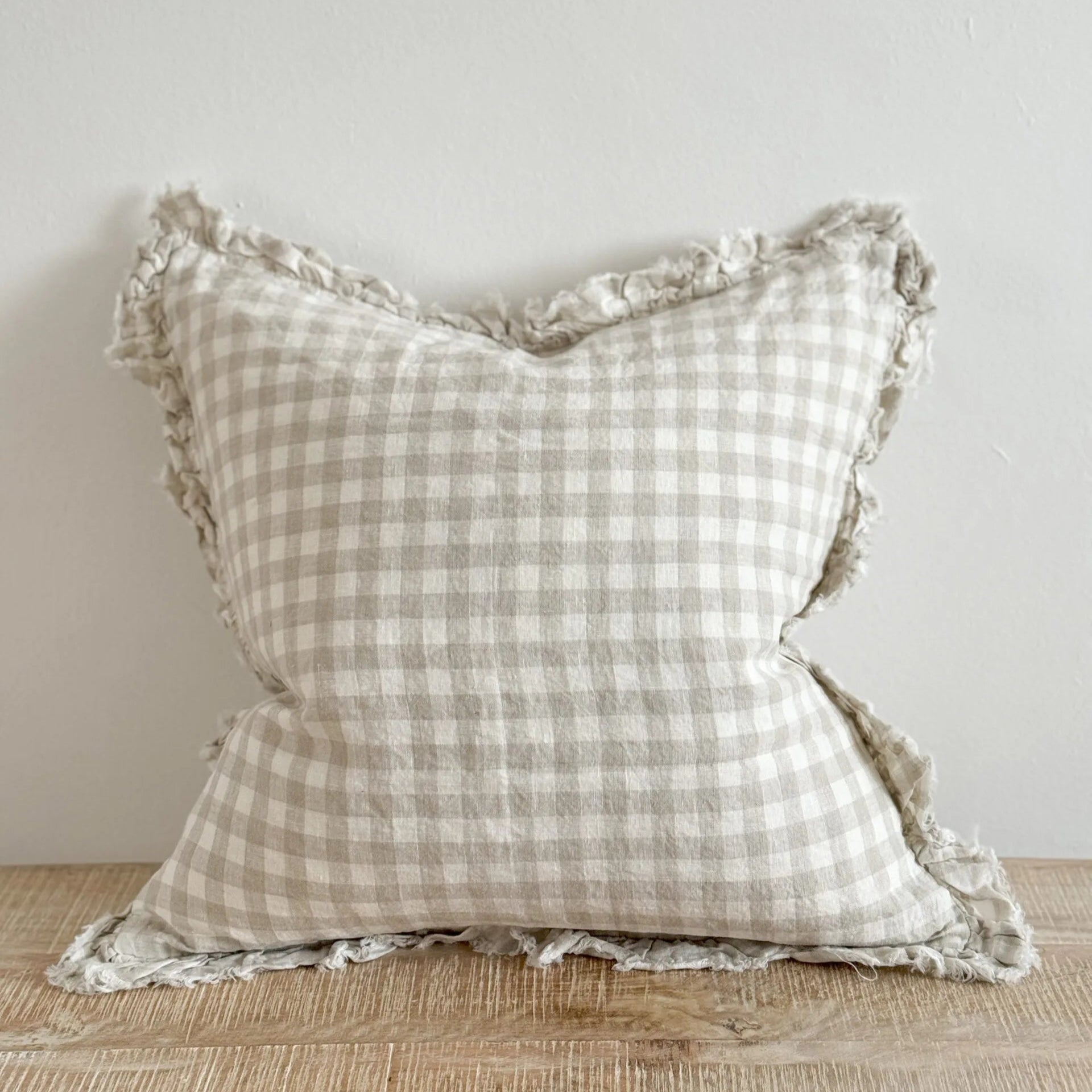 natural toned gingham cushion on wooden surface.