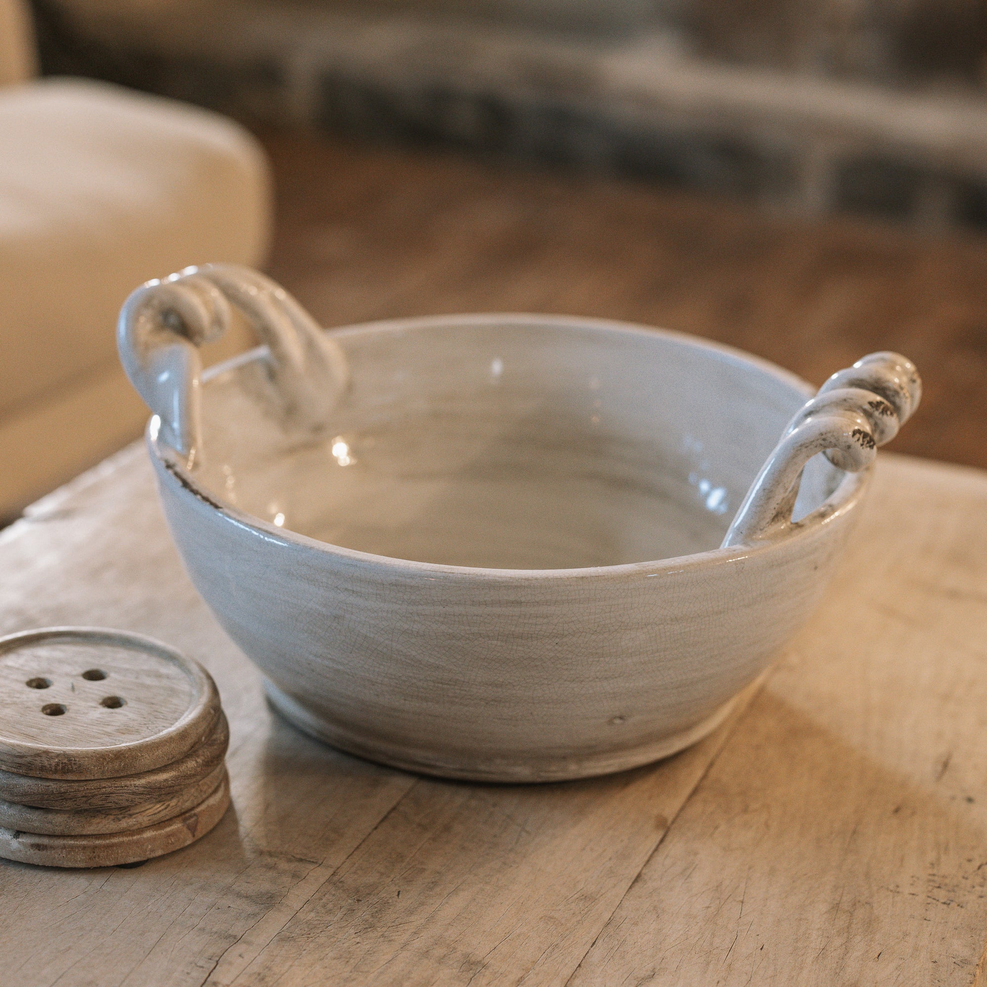 Off white ceramic bowl with twisted handles on wooden coffee table