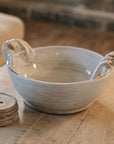 Off white ceramic bowl with twisted handles on wooden coffee table